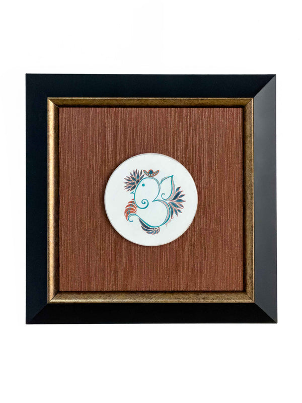 Framed circular ceramic medallion hand-painted with a teal and terracotta stylized Ganesha motif, mounted on a rust-copper textured background in a black and gold frame — Tangled Monk original hand-drawn art