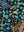 Close-up of strings of blue, sage and white dots hung on fine gold lines over black cotton duck canvas, a magenta butterfly above and a copper wing below — Tangled Monk original hand-drawn art
